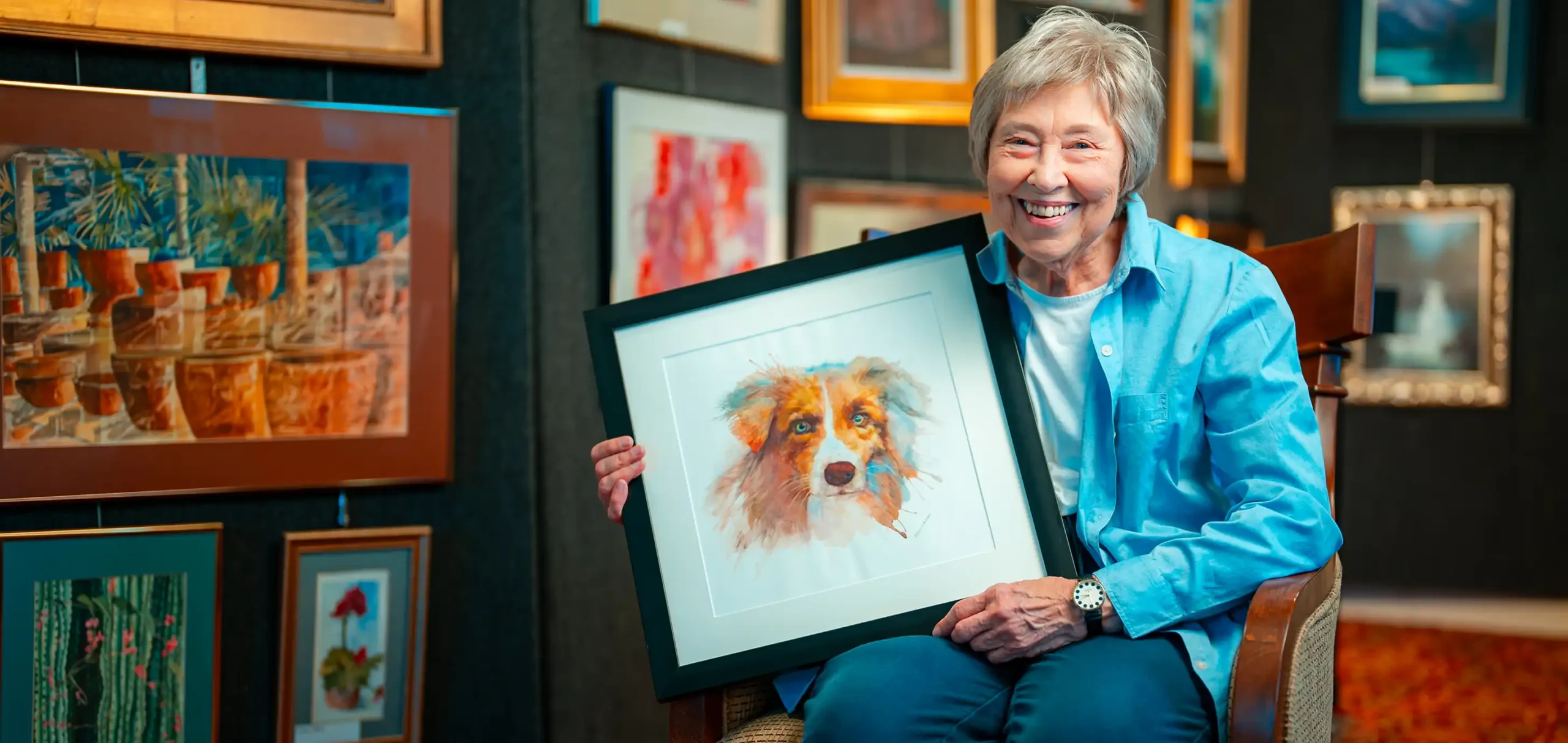 A senior woman poses with a watercolor portrait of a dog