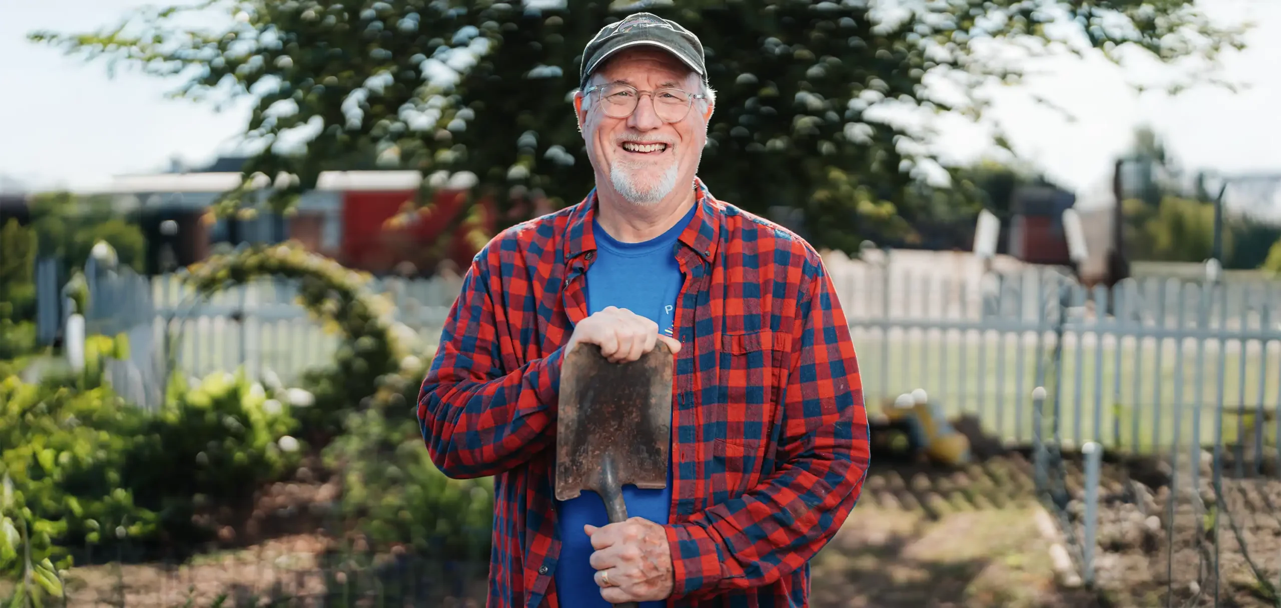 A senior man stand in a large garden with a shovel