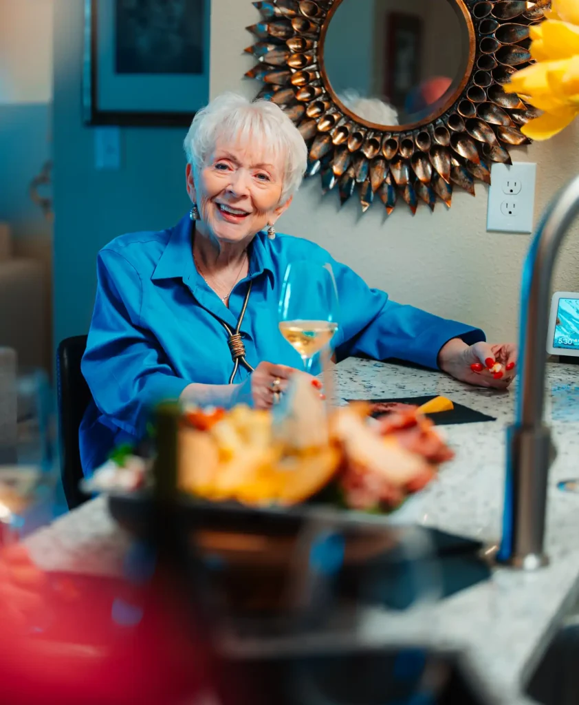 A senior woman enjoys a glass of wine with friends at a kitchen island