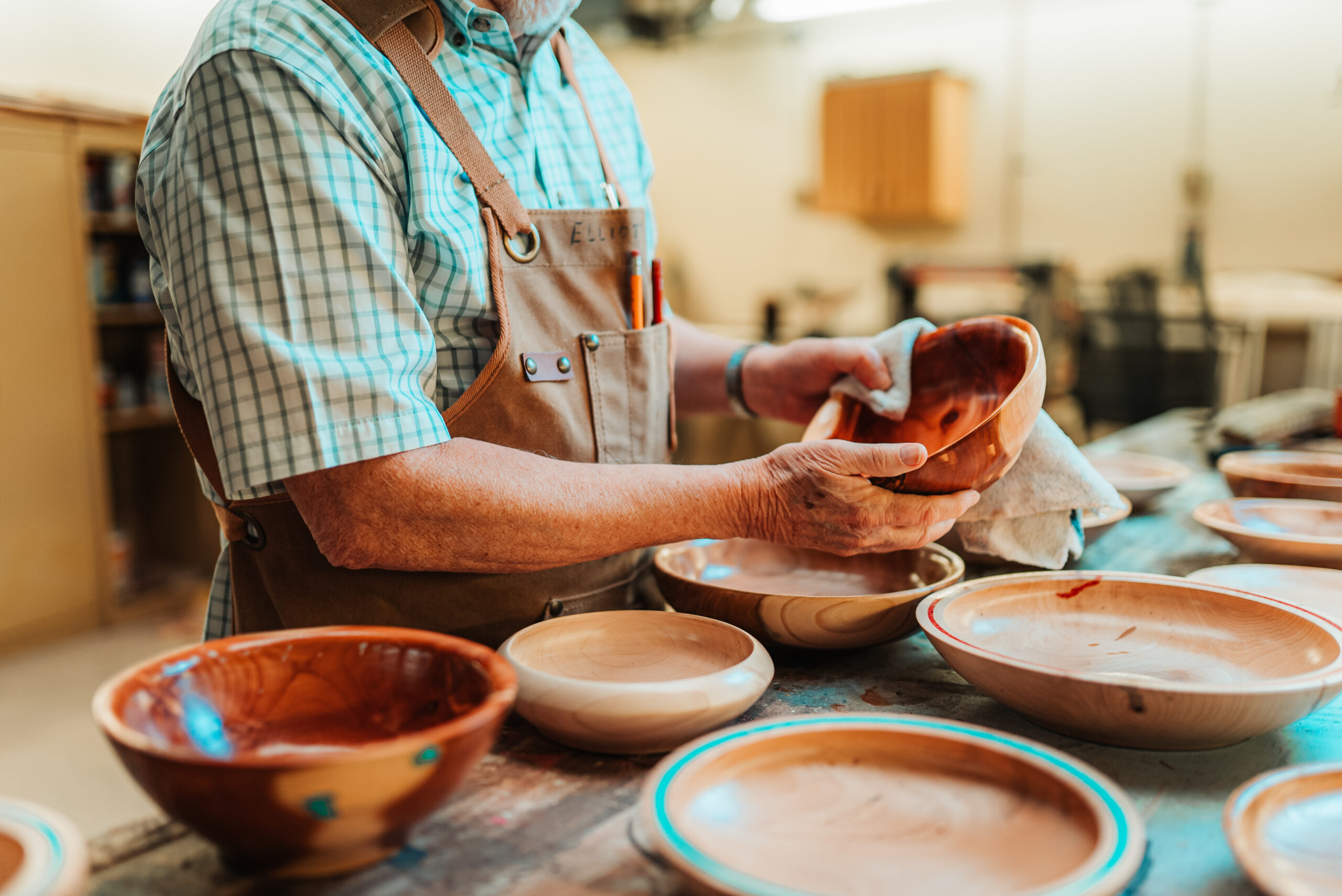 An older adult man wipes down a wooden bowl in the woodshop