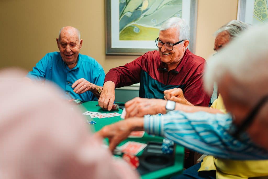 Senior residents laughing together during a card game at a green felt table