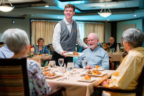 Dining staff member serving a meal to senior residents enjoying lunch together at Epworth Villa in Oklahoma City.