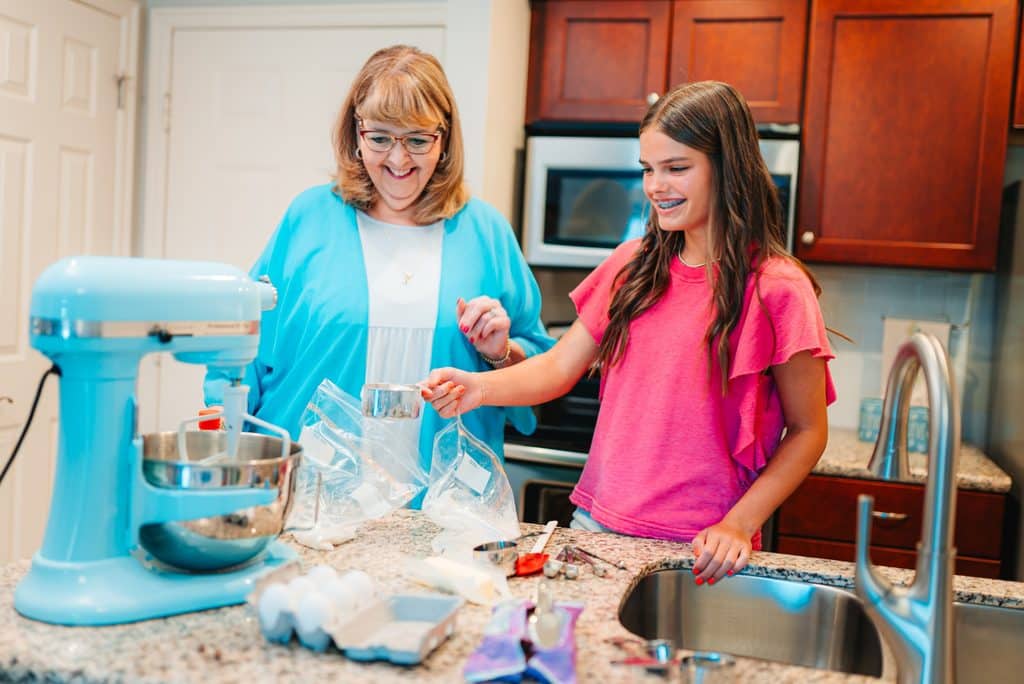 Senior woman and her granddaughter bake together in a kitchen next to a blue stand mixer