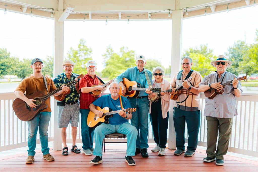 Group of senior men holding acoustic guitars pose together on a covered gazebo deck