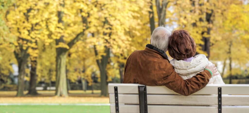 Senior couple sitting on a white park bench in autumn